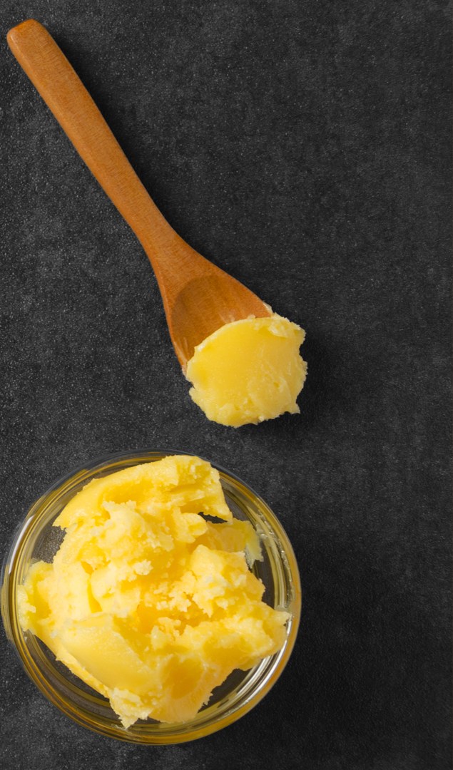 Set ghee on a wooden spoon beside an open glass jar of ghee, shot from above